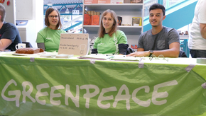 Drei Studierende der Organisation Greenpeace sitzen hinter ihrem Messestand, auf dem Flyer verteilt worden sind.