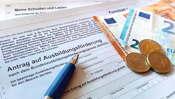 Auf einem leeren Antrag auf Ausbildungsförderung liegen ein Kugelschreiber und einzelne Euroscheine und -münzen.