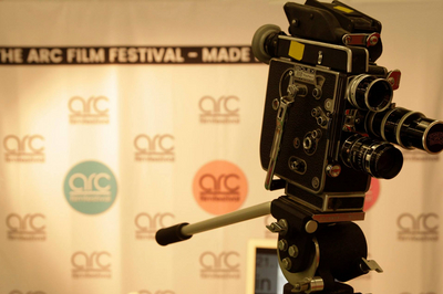 Eine Kamera. Im Hintergrund eine Werbewand, auf der "Arc Filmfestival" steht. 