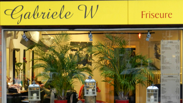 Ein Friseurgeschäft mit zwei Pflanzen und drei Laternen im Schaufenster.