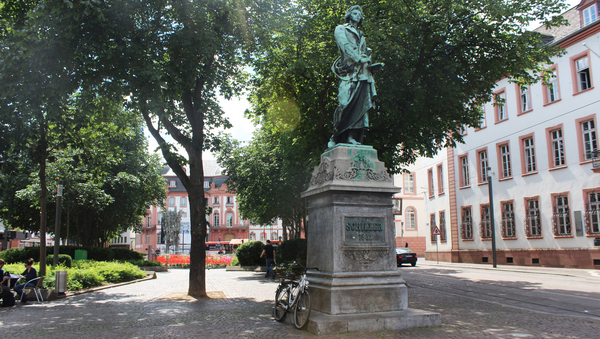 Ein Platz mit Denkmal und Brunnen im Hintergrund