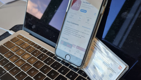 Ein Smartphone und ein Studierendenausweis lehnen an einem aufgeklappten Laptopbildschirm. Das Handy zeigt die JGU-App im App Store.