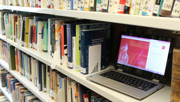 Ein Laptop steht in einem Regal der Bibliothek. 