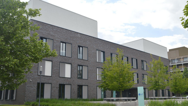 Ein großes, graues Gebäude, davor Bäume und eine Wiese.