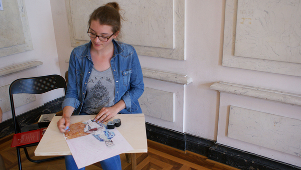 Eine junge Frau sitzt an einem kleinen Tisch und zeichnet.