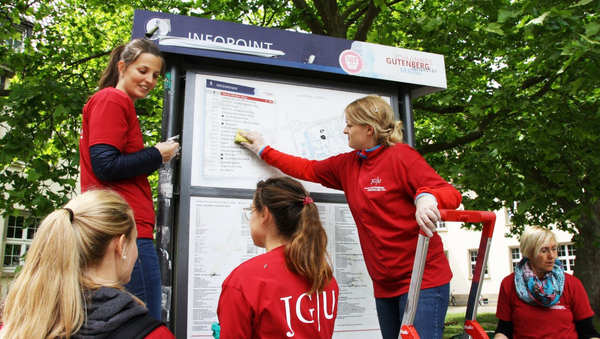 Eine Gruppe von jungen Frauen in roten T-Shirts reinigen eine Informationstafel.