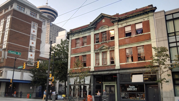 Straßenecke in Vancouver, ältere rote Ziegelhäuser, im mittigen Haus ist unten ein Lebensmittelgeschäft.
