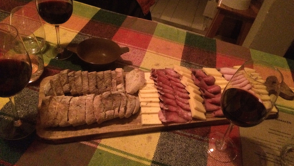 Drei Gläser Rotwein und eine Platte mit Käse und Fleisch, auf einem gedeckten Tisch.