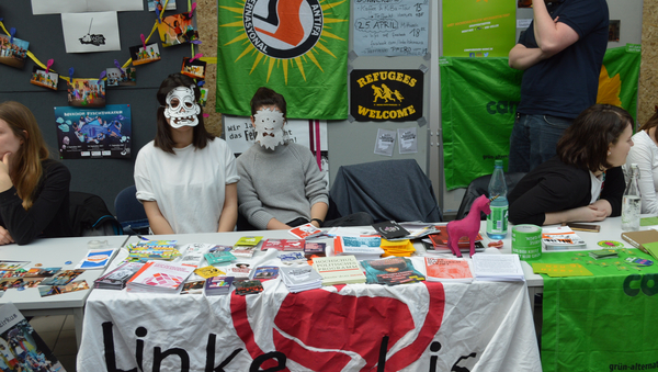 Zwei Frauen sitzen an einem Messestand. Sie tragen Papier-Masken.