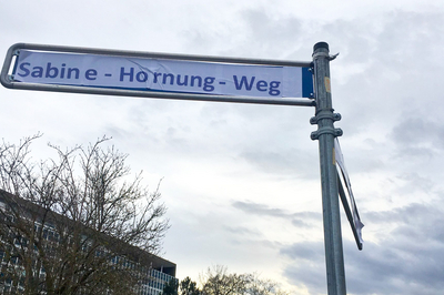 Ein Straßenschild, über das ein Schild geklebt wurde, auf dem "Sabine-Hornung-Weg" steht.