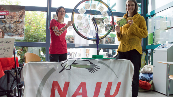 Zwei Mitglieder der Hochschulgruppe "NAJU" stehen um ein selbstgebautes Glücksrad aus einem Fahrradreifen herum und präsentieren ihren Messestand.
