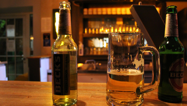 Links und rechts eine Flasche Bier, in der Mitte ein halb gefülltes Bierglas auf einer Theke. 