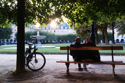 Ein Pärchen auf einer Bank in einem Park. Am Baum neben ihnen lehnt ein Fahrrad.