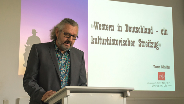 Thomas Schneider. Dahinter eine Powerpoint Folie: "Western in Deutschland - ein kulturhistorischer Streifzug" ©Filmz