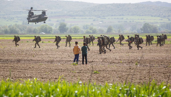 Ein Militärhubschrauber fliegt über ein Feld, am Boden sind Soldaten, einige Camp-Bewohner nähern sich. ©David Lohmüller