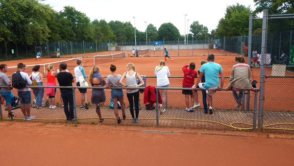 Zuschauer und Tennisspielende Personen auf zwei Tennisplätzen