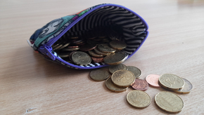 Ein offener Geldbeutel, in dem sich nur noch einige Münzen befinden, liegt auf einem Tisch.