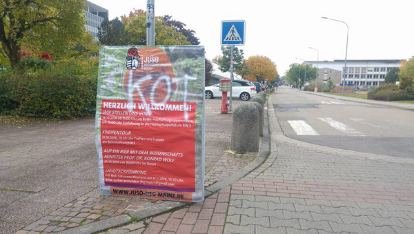 Ein Plakat der Juso-HSG, auf das mit weißer Farben das Wort "Kot" geschrieben wurde. Im Hintergrund eine Straße, Autos und Gebäude.