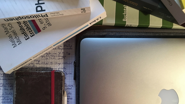 Arbeitsplatz bei Hausarbeiten: Lehrbücher, ein Laptop, ein Notizbuch erleuchtet durch eine Schreibtischlampe.