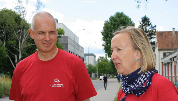 Links im Bild steht ein Mann, rechts eine Frau mit blauem Halstuch. Beide tragen rote T-Shirts.