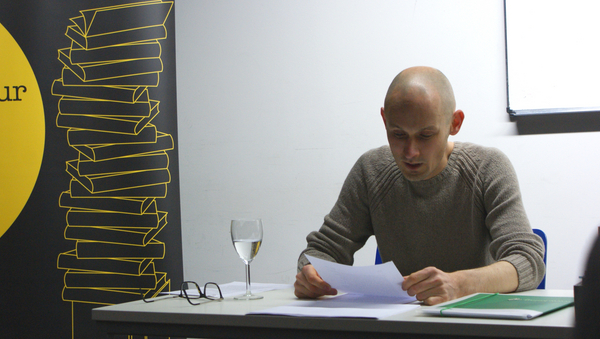 Matthias Senkel sitzt an einem Tisch und liest aus "Dunkle Zahlen".