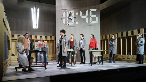 Die Darstellerinnen von "7 Minuten. Betriebsrat (DSE)" auf der Bühne des Staatstheaters Mainz. Im Hintergrund strahlt eine große Digitaluhr "18:46".