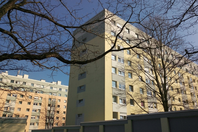 Ein Wohnungsbau vor blauem Himmel, davor Äste eines Baums.