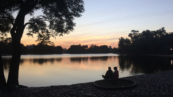 Zwei Personen sitzen an einem See, hinter dem die Sonne untergeht.
