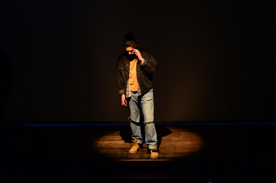 Ein Mann steht im Lichtkegel auf einer dunklen Bühne.