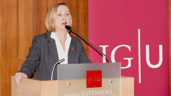 Eine Frau hält eine Rede. Im Hintergrund ein roter Banner der Uni Mainz.