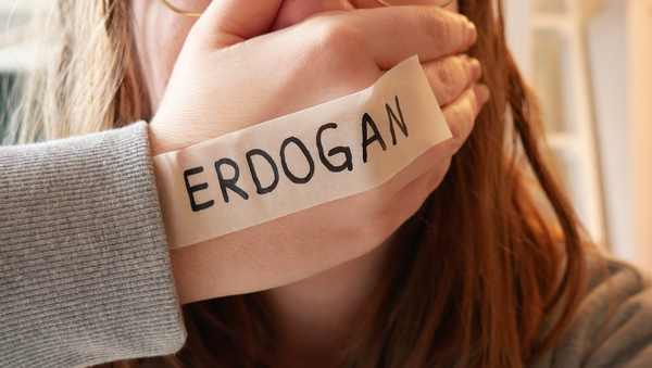 Eine junge Frau schlägt sich die Hand vor den Mund. Auf ihrem Handrücken steht "Erdogan" in schwarzer Schrift.