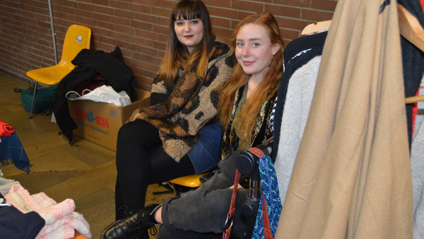 Blick vorbei an einer Kleiderstange auf zwei Mädchen, die nebeneinandersitzen und lächeln