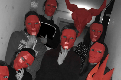 Eine Gruppe von Menschen mit roten Masken, die in die Kamera schauen. Eine Person trägt eine Teufelsmaske.