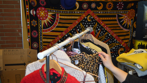 Kleiderstange vor Wand, die mit buntem Tuch abgehängt wurde und Hand, die nach Kleidungsstück auf der Stange greift