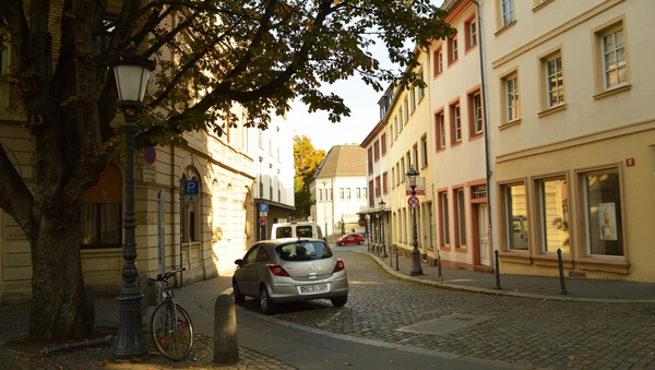 A street in the historic center. At the left and the right side houses. On the left a tree. On the street a parking car. 