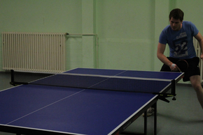 Student steht an einem Tischtennistisch und schlägt mit einem Tischtennisschläger gegen den kleinen Ball