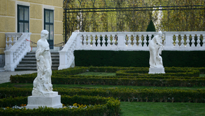 Zwei antike Statuen stehen mit Abstand in einem Park.