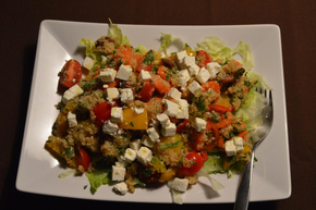 Quinoa-Salat mit Gemüse und Schafskäse auf einem weißen viereckigen Teller mit einer Gabel. Von oben aufgenommen. 