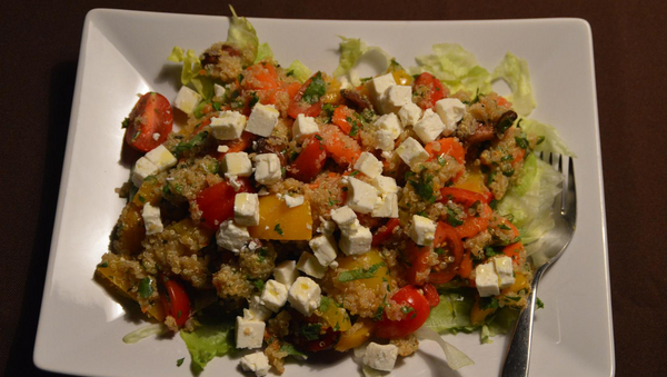 Quinoa-Salat mit Gemüse und Schafskäse auf einem weißen viereckigen Teller mit einer Gabel. Von oben aufgenommen. 